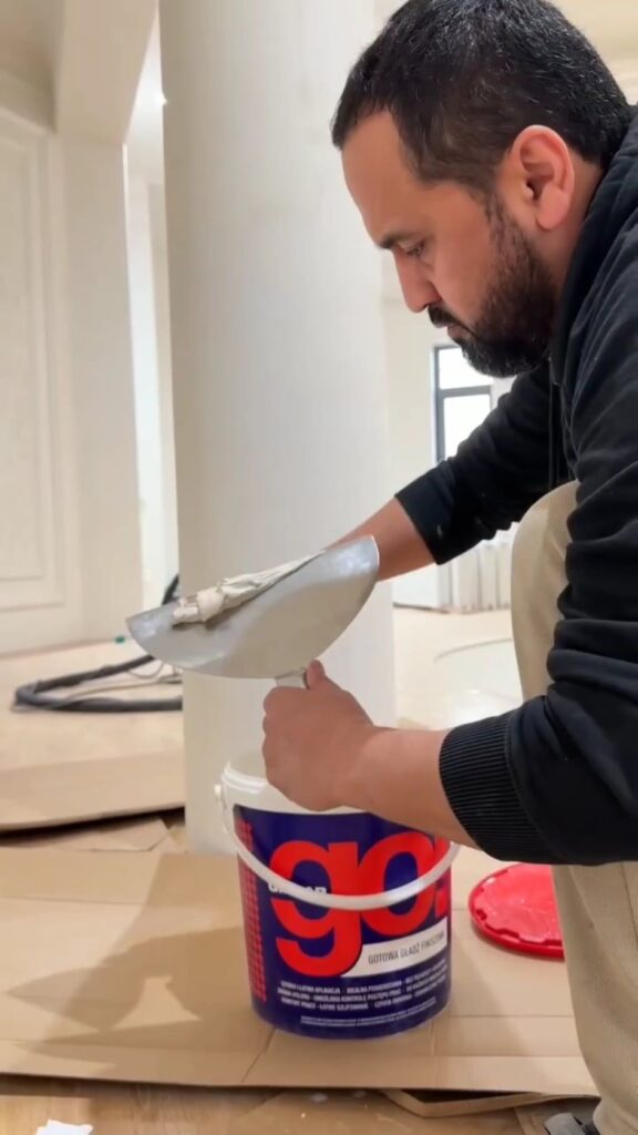 バケツからパテをすくい出す男性