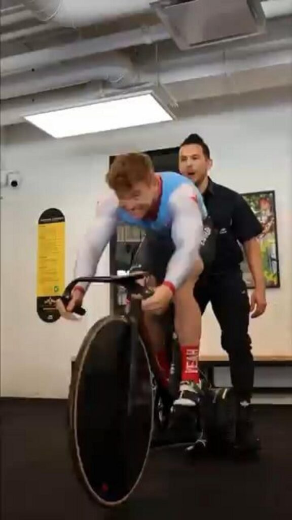 全力で自転車を漕ぐ男性と見守るコーチ