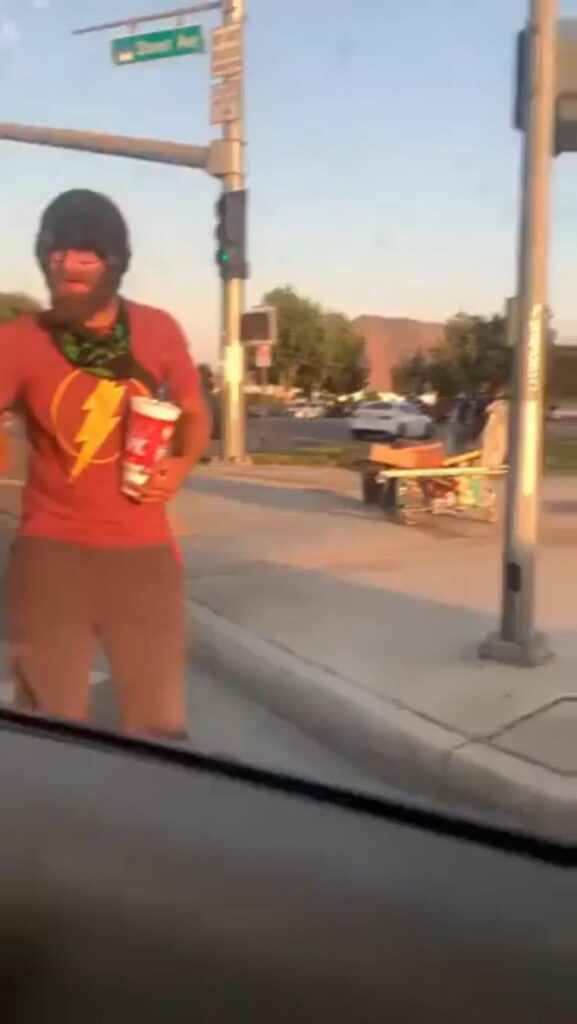 飲み物を持ち道路脇に立つ赤い服の男性