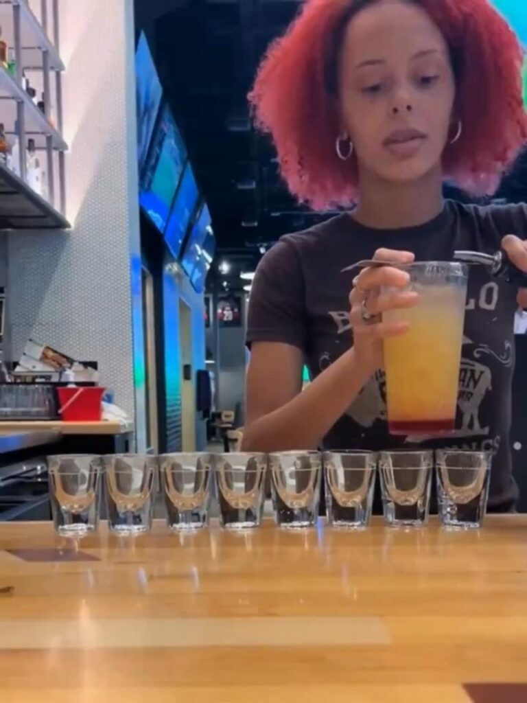 ショットグラスに酒を注ぐ赤い髪の女性