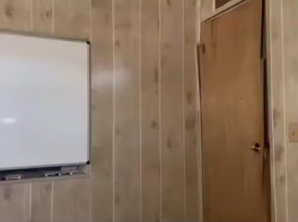 木目調の壁にホワイトボードとドアがある