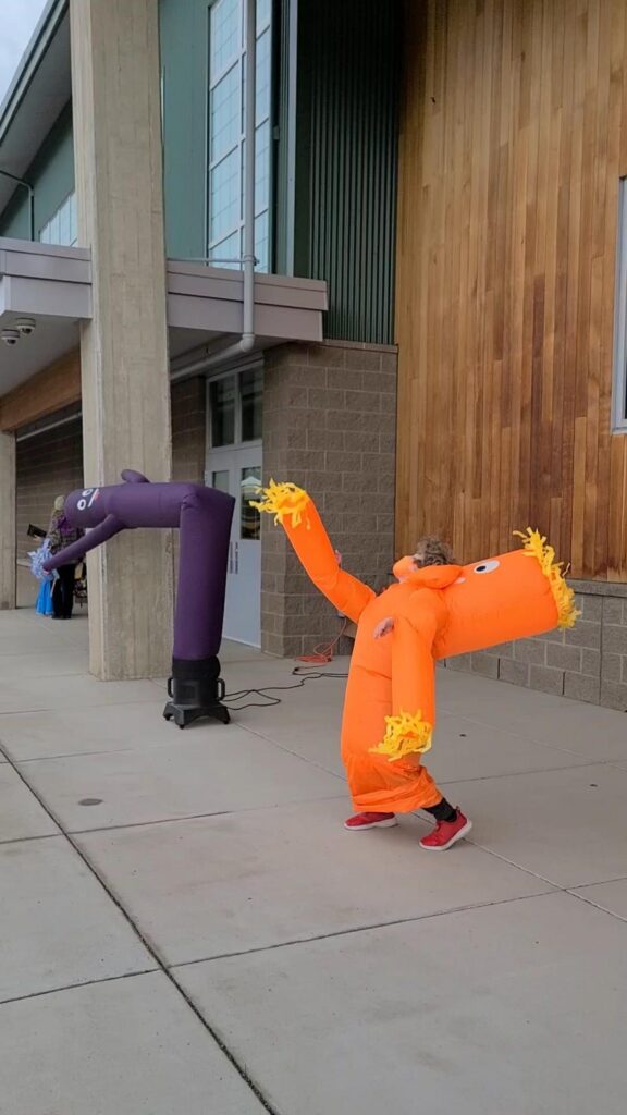 エアー看板を真似るオレンジの着ぐるみの人