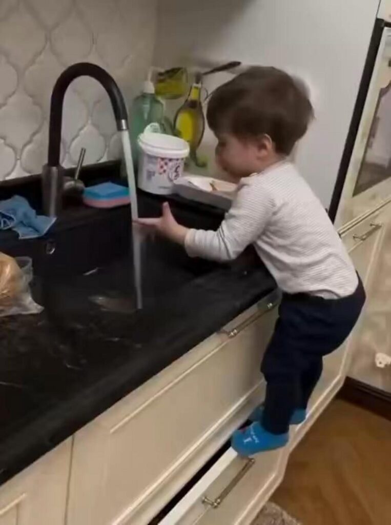 引き出しに立ち水道で遊ぶ幼い子供