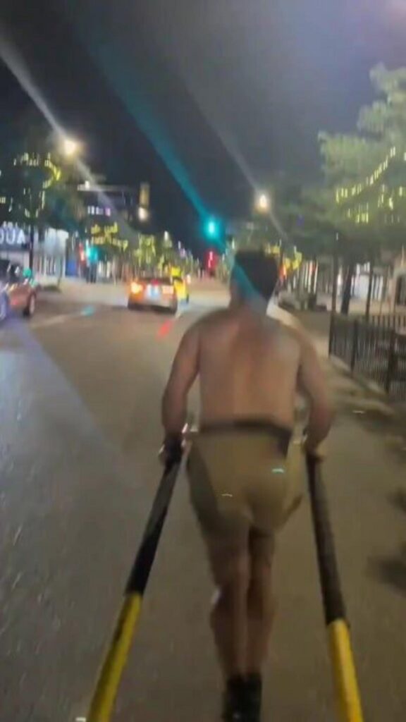 夜の街で半裸の男性が長い棒を使い移動する