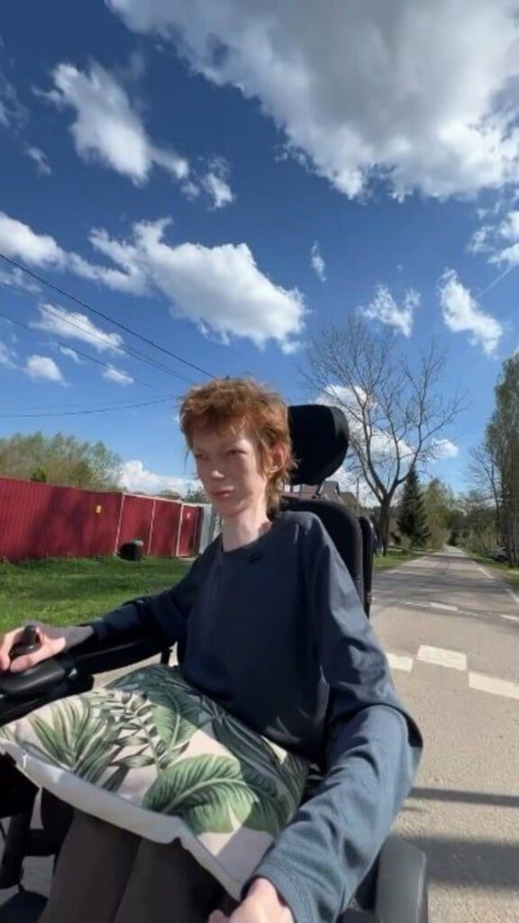 青空の下で電動車椅子に乗る赤毛の人物